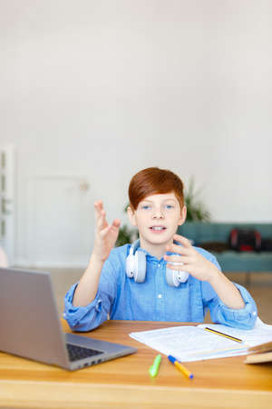 Vertical photo of a pupil boy during an online call with classmates or a teacher. He does his...