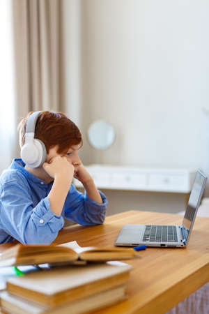 Vertical photo sad boy pupil in headphones in front of a laptop monitor during an online lessonの写真素材