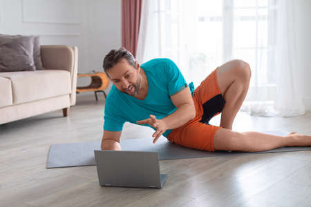 Yoga coach during an online video call. He communicates with the client explaining the exercise and...