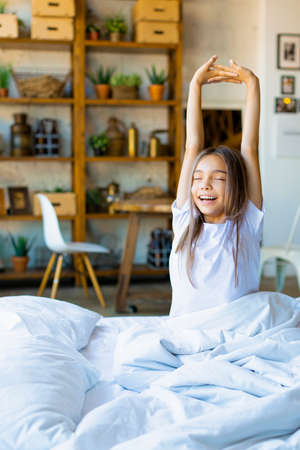 Vertical photo of a ten-year-old girl woke up and, stretching. She stretched her arms up and enjoys the day off.の写真素材