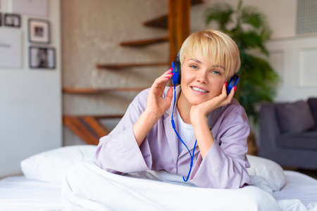 Smiling woman in bed wearing headphones. She woke up and listens to her favorite music.の写真素材