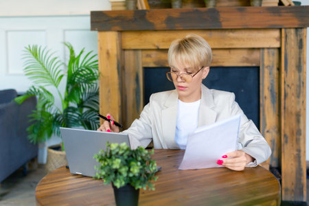 Woman in glasses works with documents in front of a laptop monitor. She checks the tax records...
