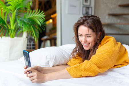 Vertical photo. woman lies in bed with cell phone. She woke up and was checking social media posts.