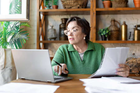 A mature woman while filling out documents. She uses an online tutorial to fill in the documentation correctly.の写真素材