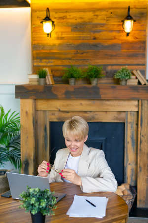 Vertical photo of a young blonde in front of a laptop. She smiles during an online video call with...