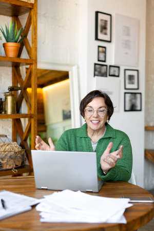 Vertical photo of a smiling senior woman filling forms online in home interior. She having online...