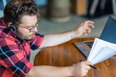 Man works with documents in front of a laptop monitor in home interior. She checks the tax records...