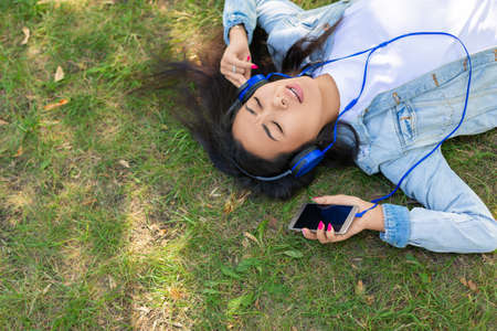 Asian woman enjoying the music while lyuing on the grass in city park - view from the top.の写真素材