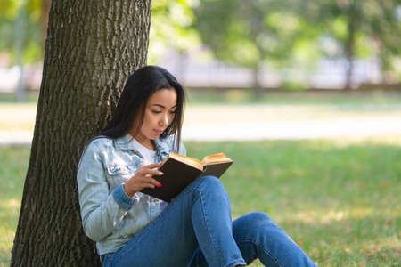 Asian woman with a book under the tree in the park. The digital detox concept.