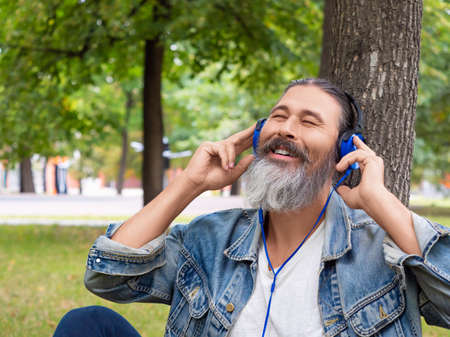 Middle-aged man enjoying the music while sitting on the grass in city park - vertical photo.の写真素材
