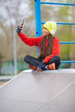 A ten-year-old girl in white headphones takes a selfie on a smartphone to send to friends.の写真素材