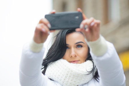A beautiful young woman makes a photo using a mobile phone.の写真素材