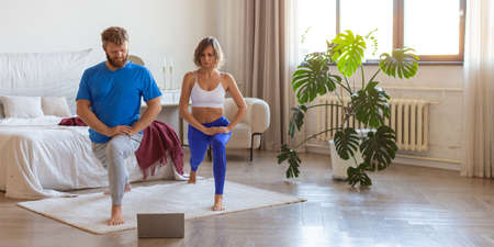 Middle-aged couple working out at homeunder the guidance of an online trainer in front of a laptop...