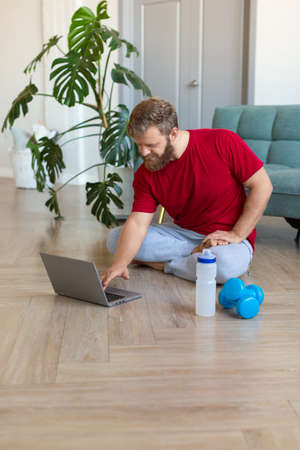 Middle-aged man picking up an online workout guide for his home workout. Vertical photo.