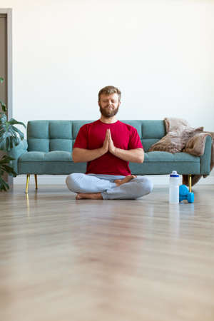 Yoga practice at home - middle aged man meditating while doing yoga. Full-length vertical photo.の写真素材