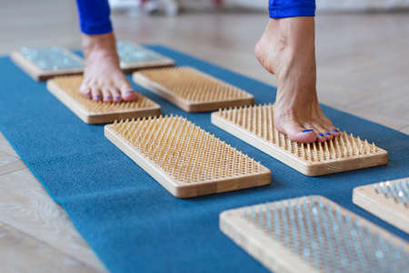 Female feet stand on a board with sharp nails over white background. Sadhus board - practice yoga. Pain, trials, health, relaxation, cognition.の写真素材