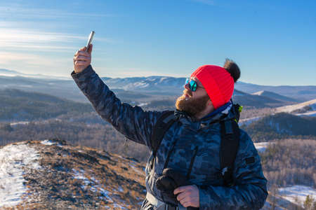 Bearded male tourist takes a selfie on the top of the mountain.の写真素材