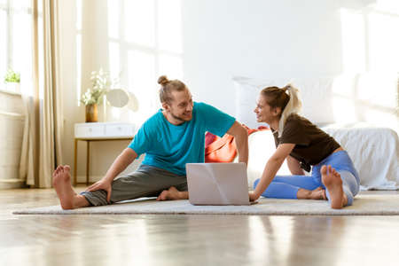 Young couple chooses an online stretching or yoga workout program at home in front of a laptop...