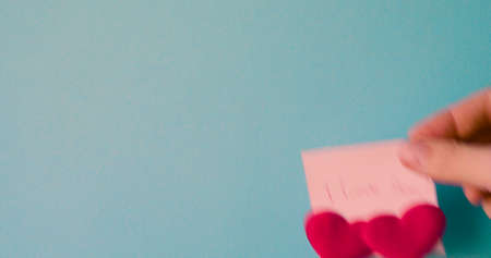 Male hand is pasting sticker with the words I love you written in pen and pasted two hearts for valentines day on a blue background.の写真素材