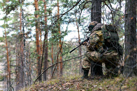 Military invasion - a soldier during a clash in the forest on enemy territory. He aims at the enemy from an ambush. Concept of modern warfare and special forces.の写真素材