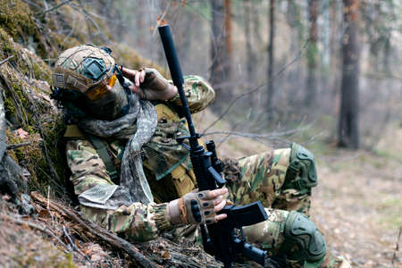 Special forces soldier during a clash in the forest. He calls his groups support on the walkie-talkie. Concept of modern military operations.の写真素材