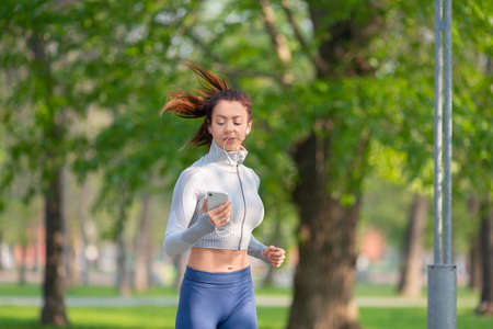 Young woman running in the city park in early morning. Attractive looking woman keeping fit and...