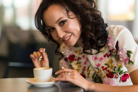 Portrait of a young Asian woman in a cafe. She smiles and is about to drink coffee.