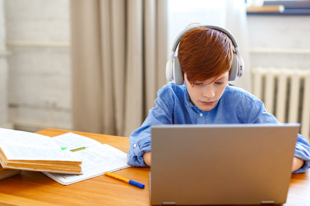 Pupil boy during an online lesson in front of a laptop monitor. He writes an online message to the teacher.の写真素材