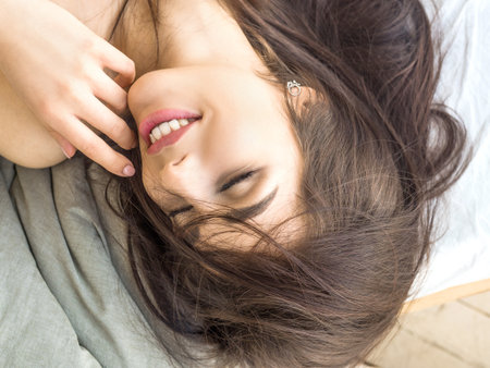 Photo of a beautiful young woman lying in bed. She smiles with closed eyes.の写真素材