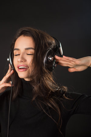 Vertical photo of a loudly singing woman listens to music in headphones and on a dark background.の写真素材