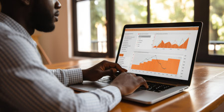 Trading cryptocurrency and securities. An African American financial analyst in glasses works in front of a laptop monitor. Track quotes in real time.の素材