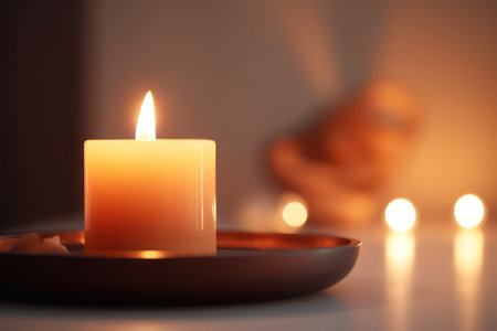 Aromatic candle burns on table in spa procedure salon. Small warm flame creating coziness and relaxing atmosphere in meditation studio. Accessory for aromatherapy treatment and mindfulnessの素材