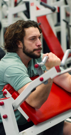 A focused workout session in vertical photo of a Caucasian man targets his biceps on a Scott bench...