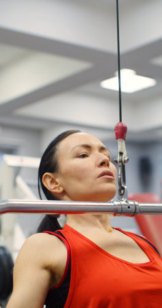 Fitness woman working out pulldown training at gym. A woman doing exercise on a lat machine in the...