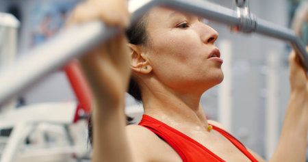 Close-up of a fitness woman working out pulldown training at gym. A woman doing exercise on a lat...