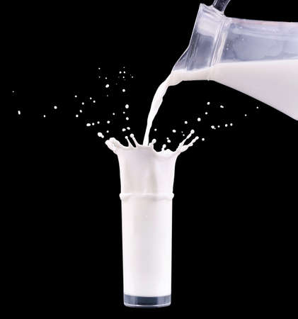 Milk is pouring from jug bottle into the glass with splash on black background.の写真素材