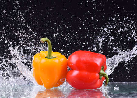 Macro drops of water fall on the red and yellow pepper and make splash