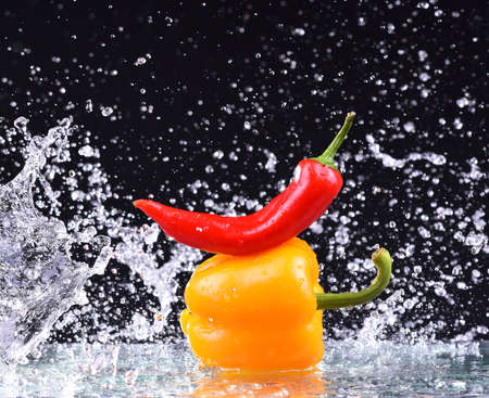 Macro drops of water fall on the red and yellow pepper and make splashの写真素材