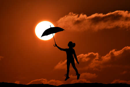 Silhouette of umbrella woman jump and sunset with big sun, landscapeの写真素材