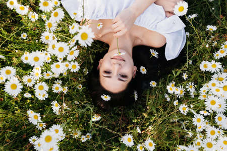 The beautiful woman lies in the field of chamomilesの写真素材