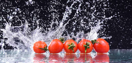 Macro drops of water fall on the red cherry tomatoes and make splash