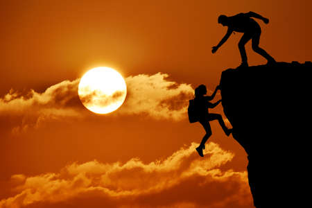 The joint work teamwork of two people man and girl travelers help each other on top of a mountain climbing team, a beautiful sunset landscape.の写真素材