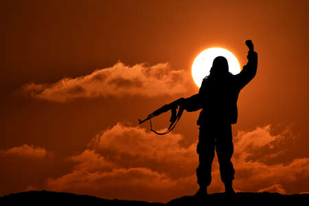 Silhouette of military soldier or officer with weapons at sunset. shot, holding gun, colorful sky, mountain, backgroundの写真素材