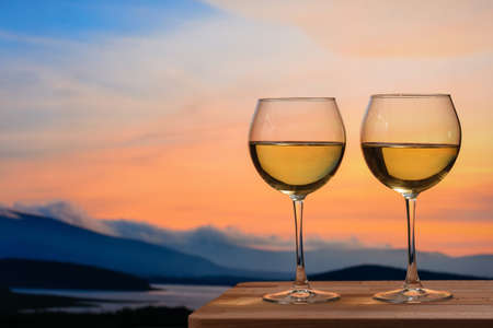Romantic glass of wine sitting on the beach at colorful sunset. Glasses of white wine against sunset, white wine on the sky background with cloudsの写真素材
