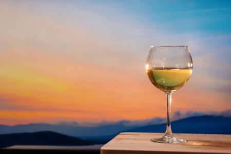 Romantic glass of wine sitting on the beach at colorful sunset. Glasses of white wine against sunset, white wine on the sky background with cloudsの写真素材