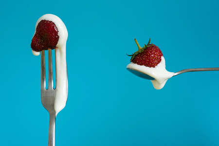Macro shot of ripe strawberries on a fork with sour cream. Closeup red berry on a spoon. Blue...