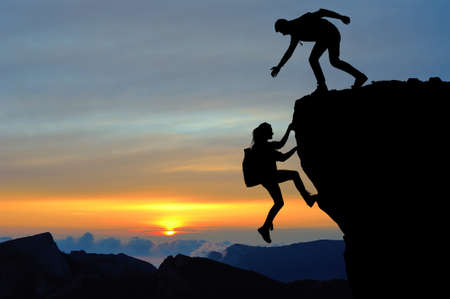 The joint work teamwork of two people man and girl travelers help each other on top of a mountain climbing team, a beautiful sunset landscape.の写真素材