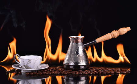 Fired cup of coffee with coffee beans and turk on dark backgroundの写真素材