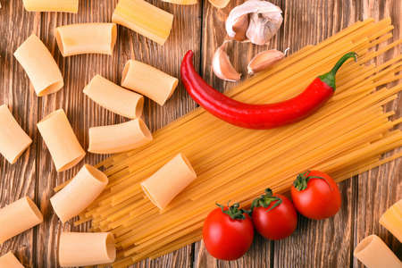 Noodles pasta pepper chili tomatoes cherry garlic on the wooden table in the kitchenの写真素材