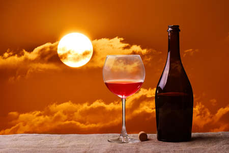 Red wine in glass, bottle and orange sunsetの写真素材